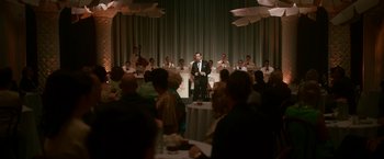 Movie still from “One Night in Miami...” (2020), directed by Regina King – A group of people sitting at a table and a man in a suit standing at a podium; Wide shot, High angle