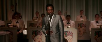 Movie still from “One Night in Miami...” (2020), directed by Regina King – A man in a gray suit standing in front of a microphone; Medium shot, Over the shoulder angle
