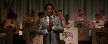 Movie still from “One Night in Miami...” (2020), directed by Regina King – A man in a suit and tie holding a microphone; Medium shot, Over the shoulder angle