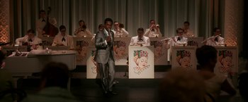 Movie still from “One Night in Miami...” (2020), directed by Regina King – A man in a gray suit standing in front of a group of people; Extreme Wide shot, Over the shoulder angle