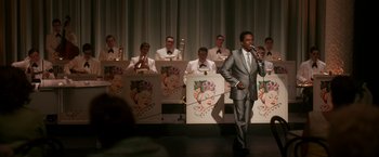 Movie still from “One Night in Miami...” (2020), directed by Regina King – A man in a gray suit is holding a microphone; Extreme Wide shot, High angle