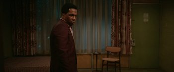 Movie still from “One Night in Miami...” (2020), directed by Regina King – A man in a suit standing next to a chair in a room; Medium shot, Over the shoulder angle