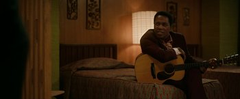 Movie still from “One Night in Miami...” (2020), directed by Regina King – A man sitting on top of a bed holding a guitar; Medium shot, High angle