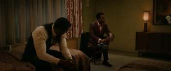 Movie still from “One Night in Miami...” (2020), directed by Regina King – A man in a suit sitting on a chair next to a bed; Medium shot, Over the shoulder angle