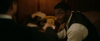 Movie still from “One Night in Miami...” (2020), directed by Regina King – A man sitting in front of a yellow phone; Close Up shot, Over the shoulder angle