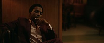 Movie still from “One Night in Miami...” (2020), directed by Regina King – A man sitting down with his hand under his chin; Medium shot, Low angle