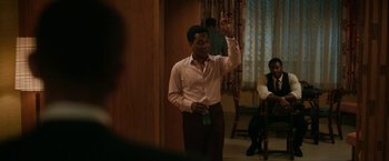 Movie still from “One Night in Miami...” (2020), directed by Regina King – A man in a white dress shirt and brown pants holds up a peace sign; Medium shot, Over the shoulder angle