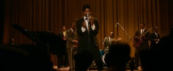 Movie still from “One Night in Miami...” (2020), directed by Regina King – A man holding a microphone while standing in front of a group of people; Medium shot, High angle