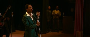 Movie still from “One Night in Miami...” (2020), directed by Regina King – A man in a green suit is holding a microphone; Medium shot, Over the shoulder angle