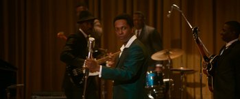 Movie still from “One Night in Miami...” (2020), directed by Regina King – A man holding a microphone in front of a group of people; Medium shot, Over the shoulder angle