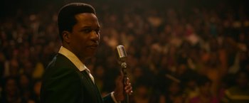 Movie still from “One Night in Miami...” (2020), directed by Regina King – A man holding a microphone in front of an audience; Close Up shot, Low angle