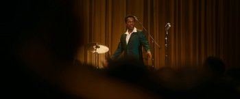 Movie still from “One Night in Miami...” (2020), directed by Regina King – A man standing on a stage in front of microphones; Medium shot, Over the shoulder angle