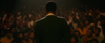 Movie still from “One Night in Miami...” (2020), directed by Regina King – A man standing in front of a crowd of onlookers; Medium shot, Over the shoulder angle