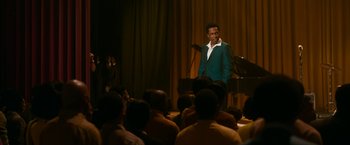Movie still from “One Night in Miami...” (2020), directed by Regina King – A man standing in front of an audience with a microphone; Medium shot, Over the shoulder angle