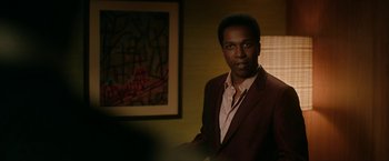 Movie still from “One Night in Miami...” (2020), directed by Regina King – A man standing in a room next to a painting; Medium shot, Over the shoulder angle