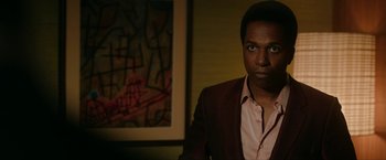 Movie still from “One Night in Miami...” (2020), directed by Regina King – A man standing in front of a painting in a dark room; Medium shot, Over the shoulder angle