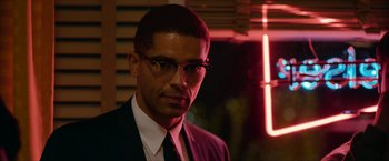 Movie still from “One Night in Miami...” (2020), directed by Regina King – A man wearing a suit and tie in front of a neon sign; Close Up shot, Over the shoulder angle
