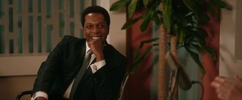 Movie still from “One Night in Miami...” (2020), directed by Regina King – A man in a suit and tie sitting next to a plant; Close Up shot, Over the shoulder angle