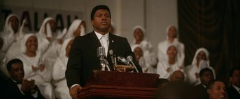 Movie still from “One Night in Miami...” (2020), directed by Regina King – A man standing at a podium with microphones; Medium shot, Low angle