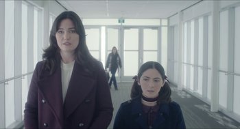 Movie still from “Orphan: First Kill” (2022), directed by William Brent Bell – Two young women standing next to each other in a hallway; Medium shot, Low angle