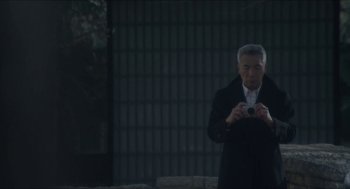 Movie still from “Orphan: First Kill” (2022), directed by William Brent Bell – An older man holding a camera in front of a brick wall; Medium shot, Low angle