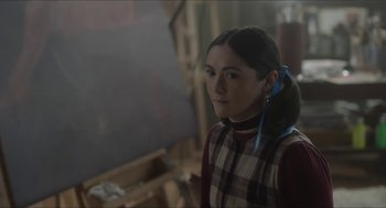 Movie still from “Orphan: First Kill” (2022), directed by William Brent Bell – A woman in a plaid shirt is standing in front of an easel; Close Up shot, Over the shoulder angle