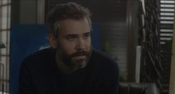Movie still from “Orphan: First Kill” (2022), directed by William Brent Bell – A man with a gray beard sitting in front of a window; Close Up shot, Over the shoulder angle