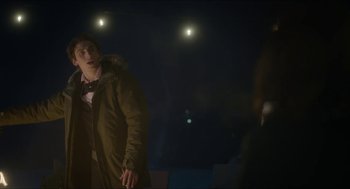 Movie still from “Orphan: First Kill” (2022), directed by William Brent Bell – A man standing in the dark wearing a coat; Medium shot, Over the shoulder angle