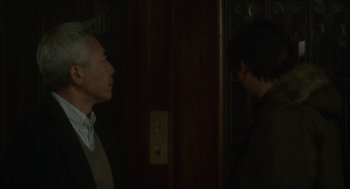 Movie still from “Orphan: First Kill” (2022), directed by William Brent Bell – Two men in suits talking in front of an elevator; Medium shot, Over the shoulder angle