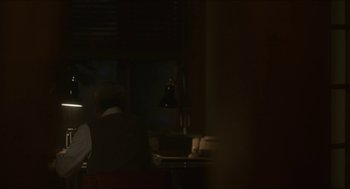 Movie still from “Orphan: First Kill” (2022), directed by William Brent Bell – A person sitting at a table in a dark room; Medium shot, Over the shoulder angle