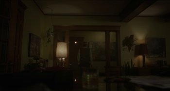 Movie still from “Orphan: First Kill” (2022), directed by William Brent Bell – A man standing in a dark room next to a lamp; Wide shot, Over the shoulder angle