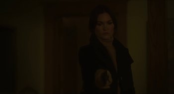 Movie still from “Orphan: First Kill” (2022), directed by William Brent Bell – A woman in a dark room holding something in her hand; Medium shot, Over the shoulder angle