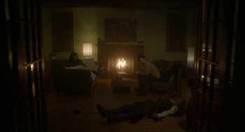 Movie still from “Orphan: First Kill” (2022), directed by William Brent Bell – A man laying on the floor in front of a fire place; Wide shot, High angle