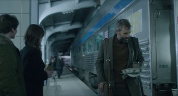 Movie still from “Orphan: First Kill” (2022), directed by William Brent Bell – A man standing next to a train on a train platform; Medium shot, Over the shoulder angle
