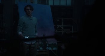 Movie still from “Orphan: First Kill” (2022), directed by William Brent Bell – A man standing in front of an easel in a dark room; Medium shot, Low angle