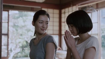 Movie still from “Our Little Sister” (2015), directed by Kore-eda Hirokazu – Two young asian women praying together in front of a window; Medium shot, Over the shoulder angle
