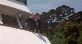 Movie still from “Overboard” (1987), directed by Garry Marshall – A man saluting on a boat with trees in the background; Wide shot, Low angle
