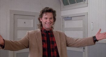 Movie still from “Overboard” (1987), directed by Garry Marshall – A man in a plaid shirt and a brown jacket smiling; Medium shot, Low angle