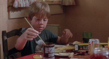 Movie still from “Overboard” (1987), directed by Garry Marshall – A young boy is sitting at a table with food; Medium shot, Low angle