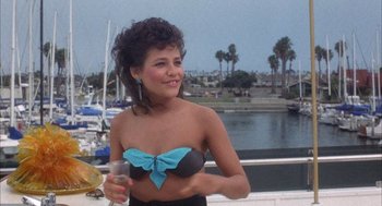 Movie still from “Overboard” (1987), directed by Garry Marshall – A woman in a black and blue bathing suit holding a glass of water; Medium shot, High angle