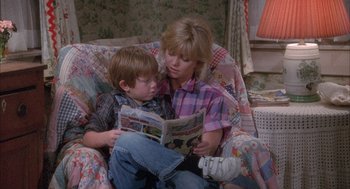 Movie still from “Overboard” (1987), directed by Garry Marshall – A woman sitting on a couch with a boy reading a book; Medium shot, High angle
