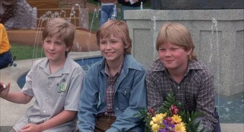 Movie still from “Overboard” (1987), directed by Garry Marshall – Three young boys sitting next to each other holding flowers; Medium shot, High angle