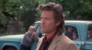 Movie still from “Overboard” (1987), directed by Garry Marshall – A man with long hair and a plaid shirt is standing in front of a blue van; Close Up shot, Over the shoulder angle