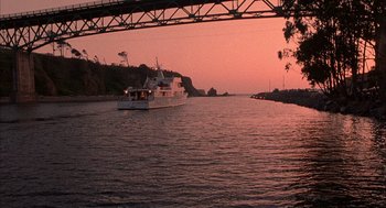 Movie still from “Overboard” (1987), directed by Garry Marshall – A boat is sailing on a body of water at sunset; Extreme Wide shot, Low angle