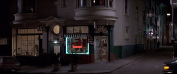 Movie still from “Mrs. Doubtfire” (1993), directed by Chris Columbus – A store front with a neon sign lit up at night; Wide shot, High angle
