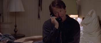 Movie still from “Mrs. Doubtfire” (1993), directed by Chris Columbus – A man talking on a phone while sitting on a couch; Medium shot, Over the shoulder angle