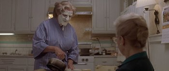 Movie still from “Mrs. Doubtfire” (1993), directed by Chris Columbus – An older woman wearing a face mask in a kitchen; Medium shot, Over the shoulder angle
