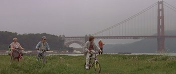 Movie still from “Mrs. Doubtfire” (1993), directed by Chris Columbus – A man riding a bike across a lush green field; Wide shot, Low angle