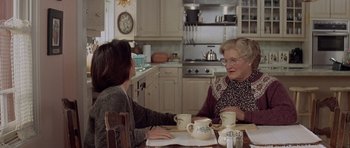 Movie still from “Mrs. Doubtfire” (1993), directed by Chris Columbus – Two women sitting at a table in a kitchen talking to each other; Medium shot, Over the shoulder angle