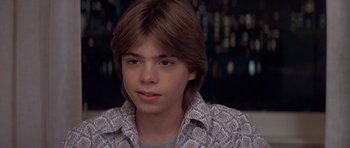 Movie still from “Mrs. Doubtfire” (1993), directed by Chris Columbus – A young man with long brown hair wearing a patterned shirt; Close Up shot, High angle